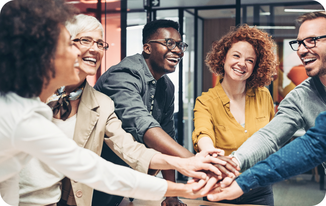 Group of smiling people standing in a circle overlap their hands in the center.