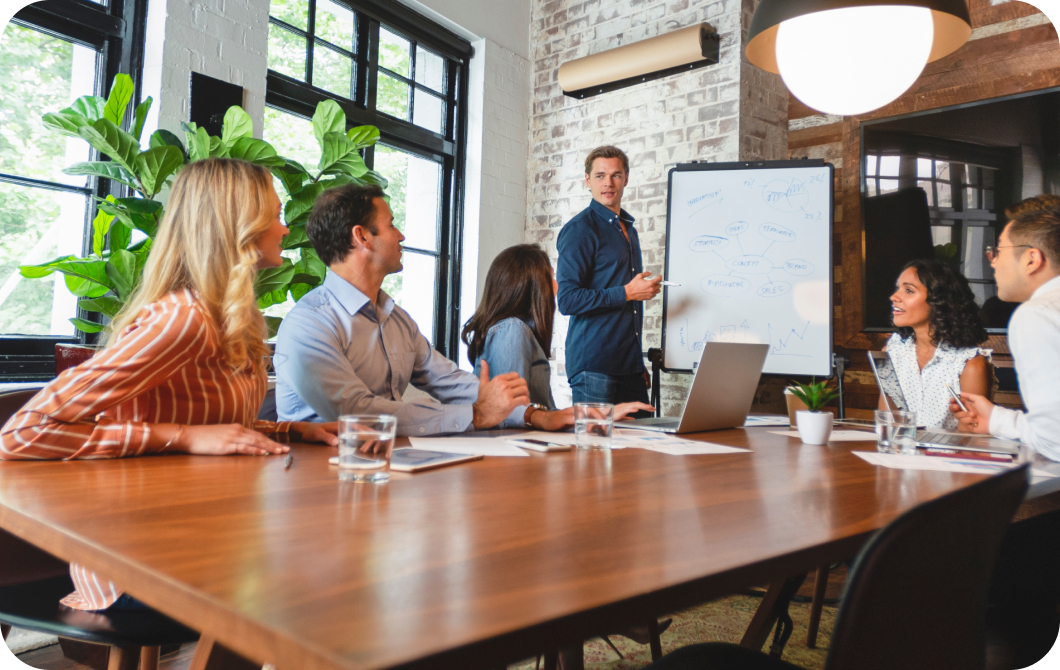 Man stands in front of a whiteboard, writing ideas on it while his seated coworkers join the converstaion.