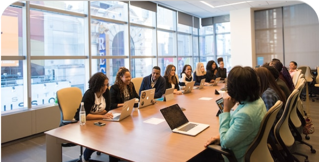 A group of professionals sit at a long table, engaged in a meeting.