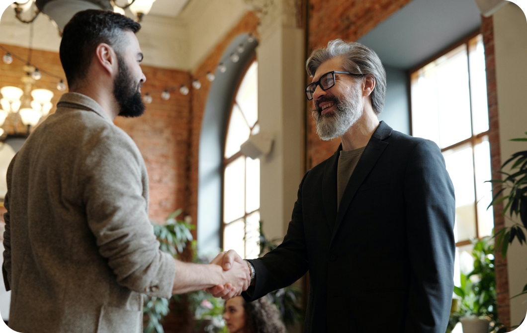 Side view of two smiling men with beards shaking hands.