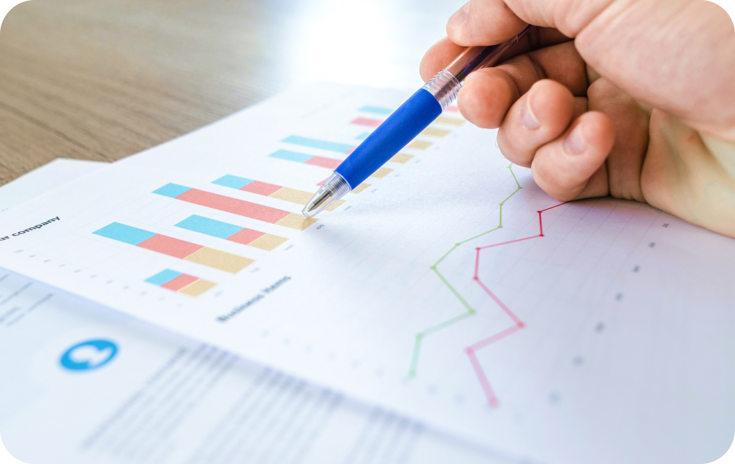 Close up of a hand holding a pen, pointing to part of a bar graph on a printed piece of paper sitting on a table.