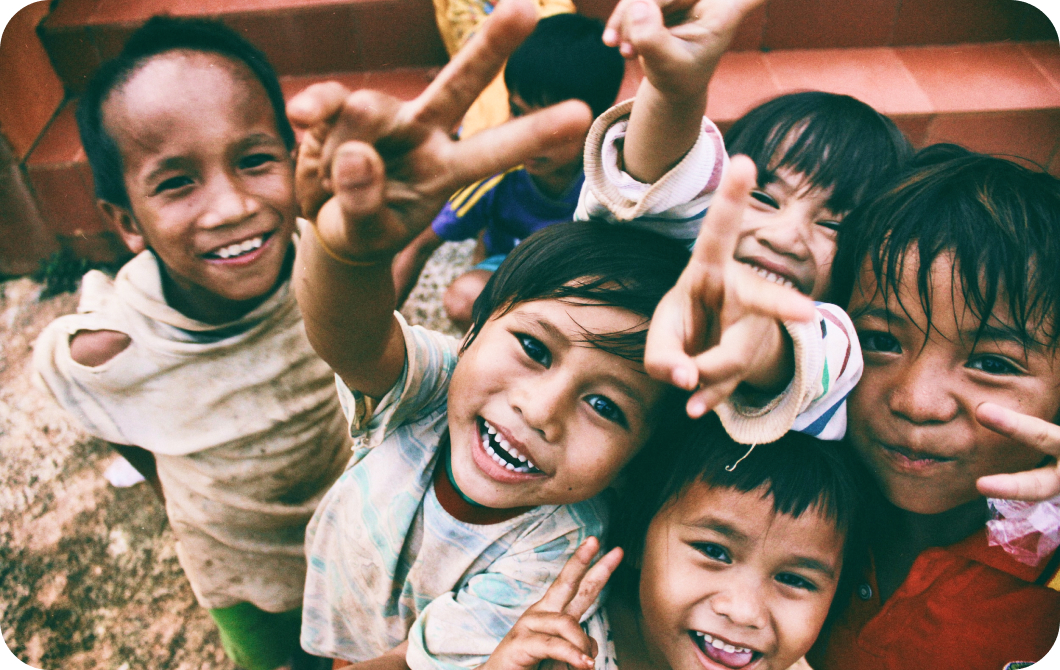 A closeup on a group of five young children smiling and giving peace signs to the camera.