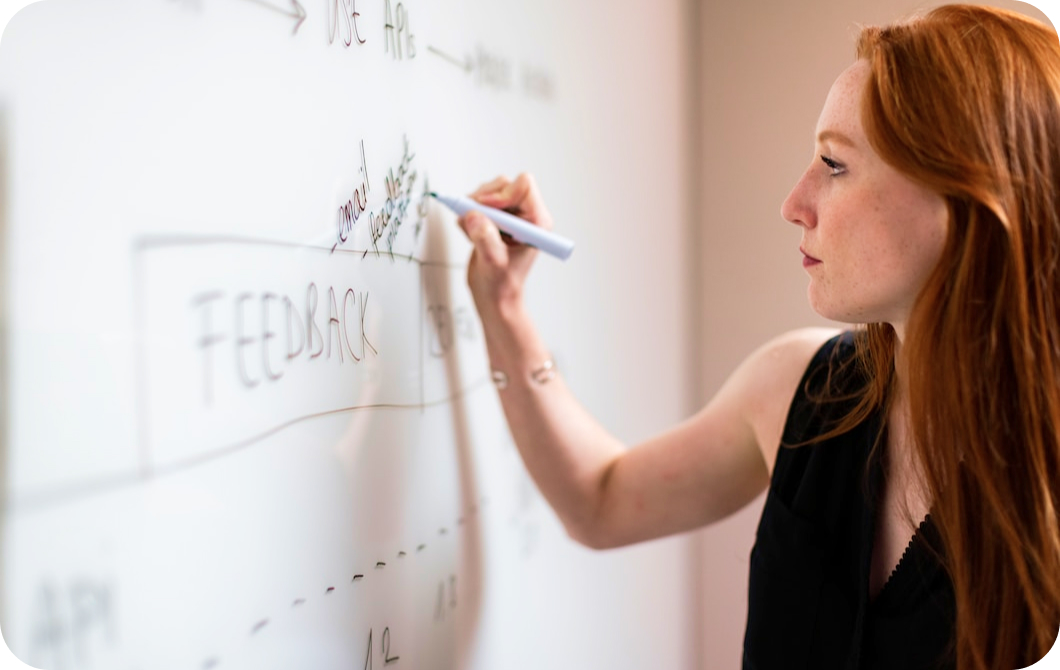 A woman intently writes notes on a whiteboard in black marker.