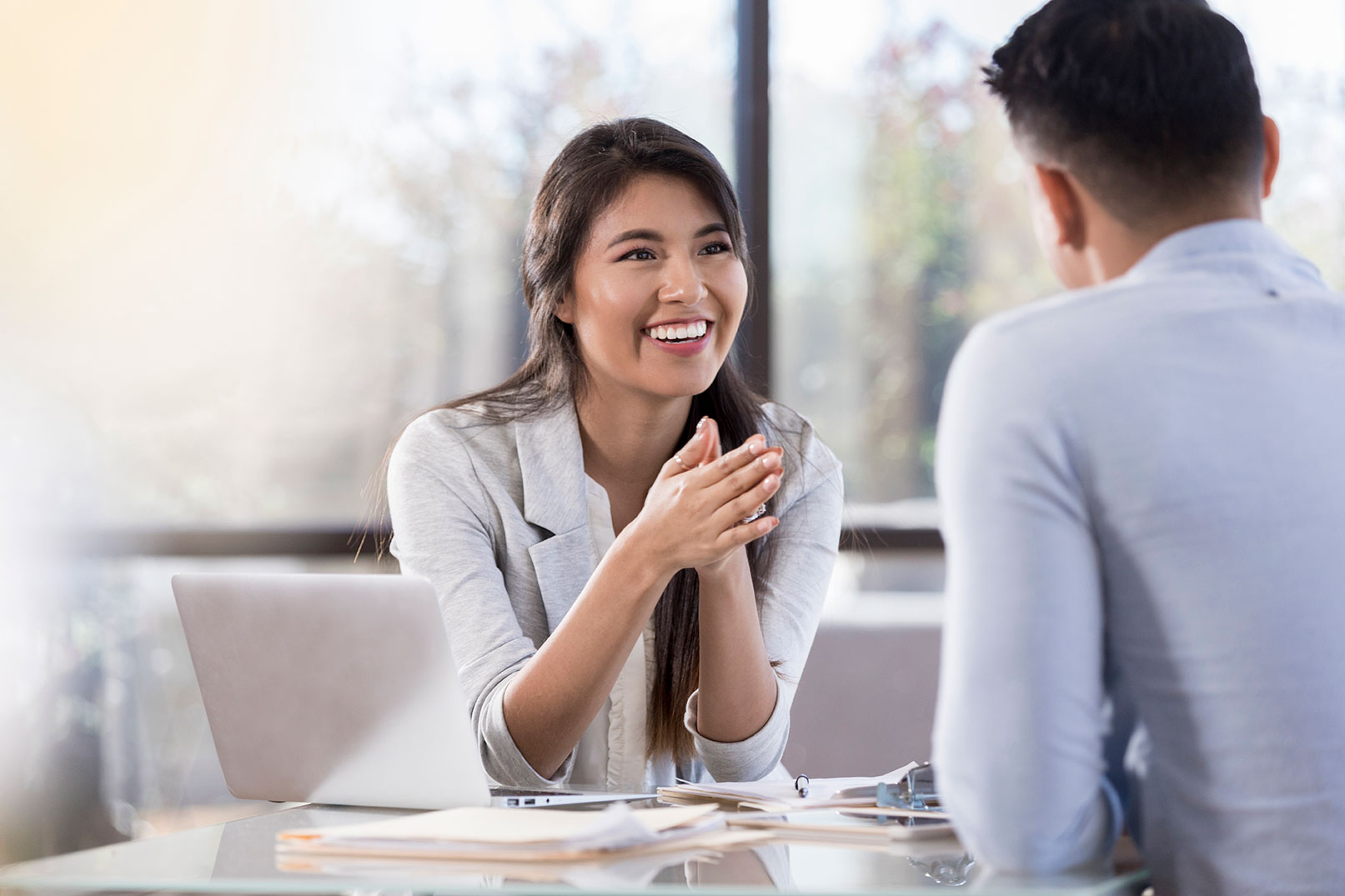 A smiling young woman rests her elbows on the table and she talks to the person sitting across from her.