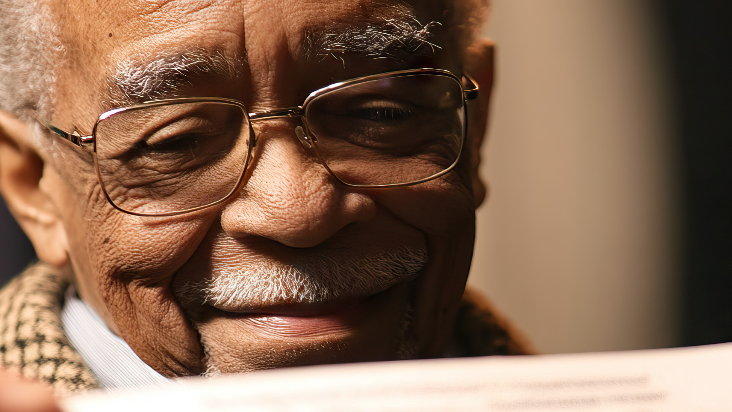 Close-up of an older man wearing glasses and smiling while reading a letter or document.